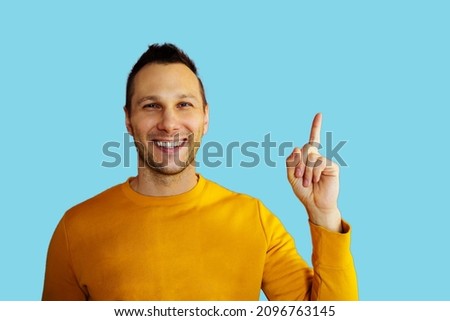 Attractive young man in yellow t-shirt pointing up with his finger isolated on blue background