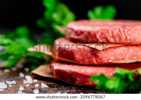Raw burger on a table with greens and salt. On a black background. High quality photo