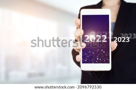 Loading year 2021 to 2022. Start concept. Hand hold white smartphone with digital hologram 2022 sign on light blurred background. Happy New Year 2022