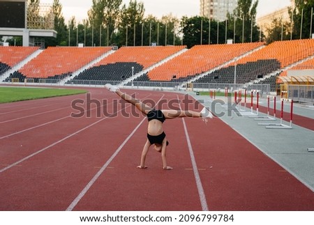 The girl is engaged in warm-up exercises and exercises in gymnastics and acrobatics in the summer at the stadium during sunset. Healthy lifestyle, sports training.