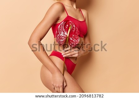 Women beauty of body. Unknown faceless woman in red cropped top and panties holds calla flower uses natural products has thin figure slender legs healthy silky skin isolated over beige background.