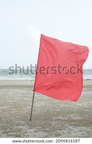 Selective focus and close up picture picture of waving red flag at the beach with strong water wave insight. In Malaysia, monsoon season is not the best time to go to the beach.