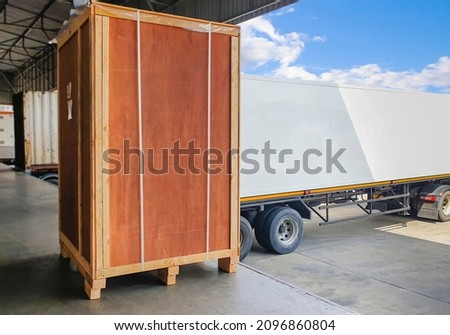 Large Wooden Crate Loading into Shipping Cargo Container. Trucks Parked Loading at Dock Warehouse. Supply Chain Shipment Logistics. Cargo Freight Truck Transport.	

