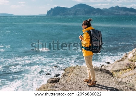 A traveler with a backpack on the background of the sea, rear view. Female traveler on the background of the blue sea, panorama. A lonely traveler on the seashore. Tourist banner. Copy space