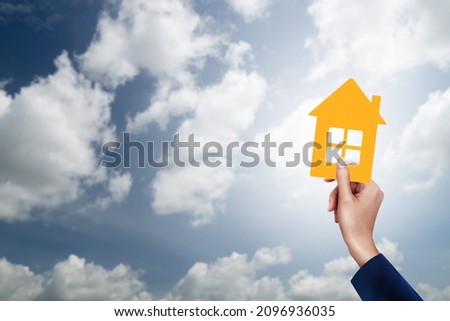 Hand holding yellow paper house on blue sunny sky background. Image of buying a house.
