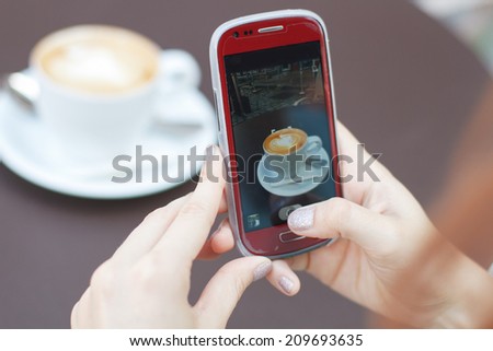 Woman taking photo of cup of coffee on her smartphone for social networks