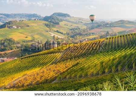 Hot air balloon flying over hills and vineyards during fall season surrounding Barolo village. In the Langhe region, Cuneo, Piedmont, Italy. Royalty-Free Stock Photo #2096938678