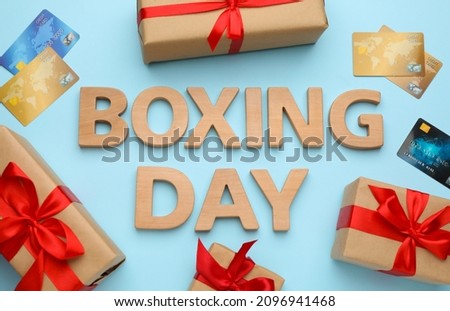 Text Boxing Day of wooden letters, credit cards and gifts on light blue background, flat lay. Sale concept