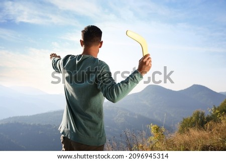 Man throwing boomerang in mountains on sunny day, back view Royalty-Free Stock Photo #2096945314