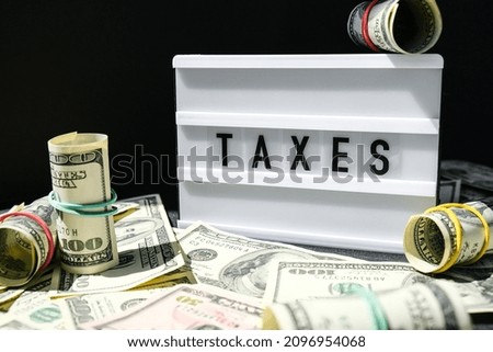 Lightbox board with word TAXES in black letters around Us dollars banknotes. Tax payment and filing concept. Money, Business, finance, investment, saving and corruption. Cash bill