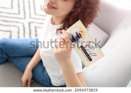 Young woman with gift certificate sitting on sofa at home