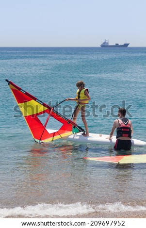 Little girl taking windsurfing lessons and pulling sail from sea water.  Royalty-Free Stock Photo #209697952