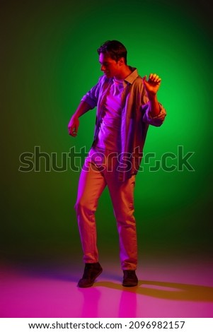 Dancer. Portrait of dancing young man, student isolated on green studio background in neon light. Concept of human emotions, facial expression, music, ad, fashion, beauty. Copy space for ad