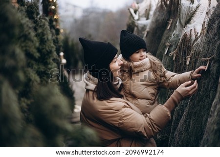 Winter holidays and people concept - happy morther and little daughter choosing christmas tree at street market. Happy family buys a Xmas tree. 