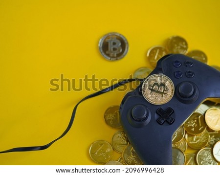 Crypto gaming. Play for earn concept. Top view of a video game controller joystick with focus on a bitcoin cryptocurrency coin on top,  gold coins underneath. Copy space. Vivid yellow background. Royalty-Free Stock Photo #2096996428