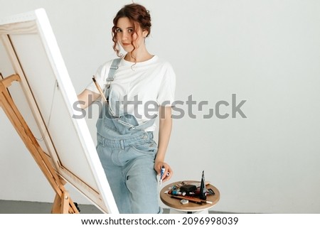 Female artist painting picture in her studio. Woman paints picture on canvas with oil paints in her studio