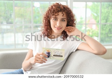Young woman with gift certificate sitting on sofa at home