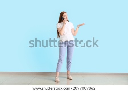 Young woman talking by mobile phone near color wall