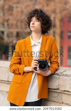 Young brunette woman with curly hair posing with her camera
