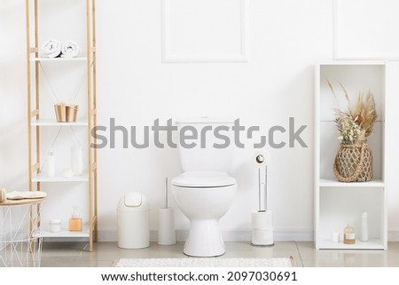 Interior of light restroom with toilet bowl, paper holder and shelf units Royalty-Free Stock Photo #2097030691
