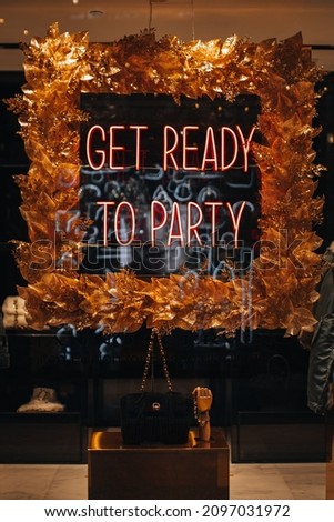 Neon shiny holiday signboard on boutique showcase with text Get ready for party.