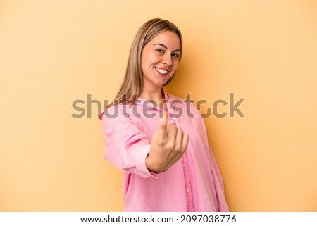 Young caucasian woman isolated on yellow background pointing with finger at you as if inviting come closer.