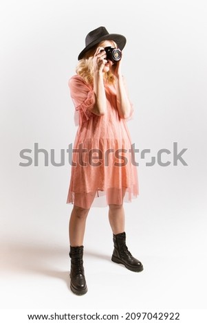 Portrait of a beautiful woman photographer in a hat posing with a camera in her hands in the studio on a white background