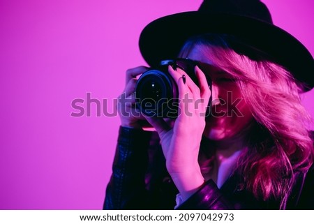 Portrait of a cute girl photographer in a hat who takes pictures in the studio on a fiolet background