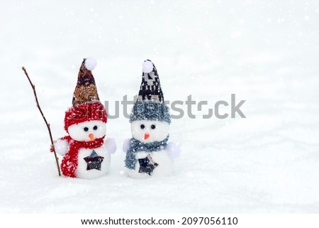Merry Christmas and happy new year greeting card with copy space Happy two little snowmen in red, blue cap and scarf standing in winter snow background Xmas fairytale Hello December, January, February