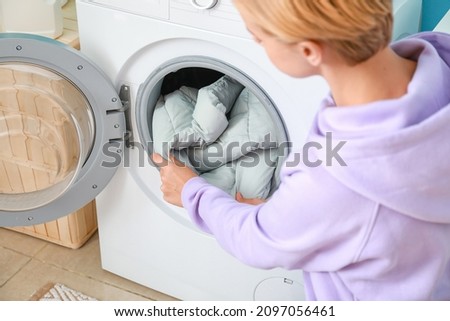 Young woman taking down jacket from washing machine in bathroom Royalty-Free Stock Photo #2097056461