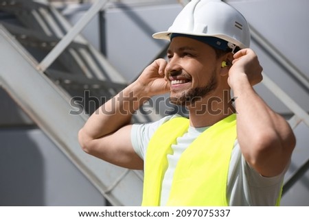 Male builder putting ear plugs outdoors Royalty-Free Stock Photo #2097075337