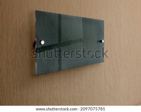 Dark green wide rectangle Transparent glass nameplate plate on spacer metal holders. Acrylic dark advertising signboard on coral background mock-up side view. Proportional 1 to 2.