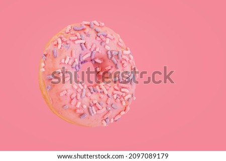 Pink donut with colorful sprinkles on pink background, copy space. Sweet food and desserts concept