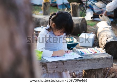 Child girl coloring picture outdoors in a summer park. Creative leisure for little child in the park. Development of the child's creativity.