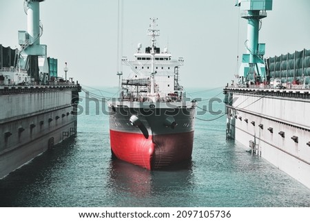  Shipyard The bulk carrier general cargo ship in dry dock yard, navigation bridge deck, recondition of hull repairing and repainting, working in dry dock yard on teal and orange. Royalty-Free Stock Photo #2097105736