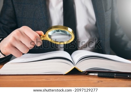 a man in a business suit examines a book with a magnifying glass