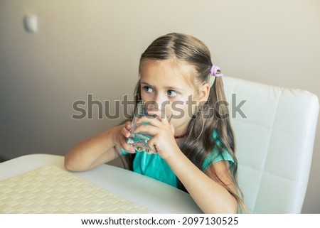 Beautiful little girl drinks clean water from a transparent glass.
