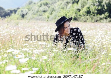 a beautiful woman in a black dress walks through a field with flowers daisies