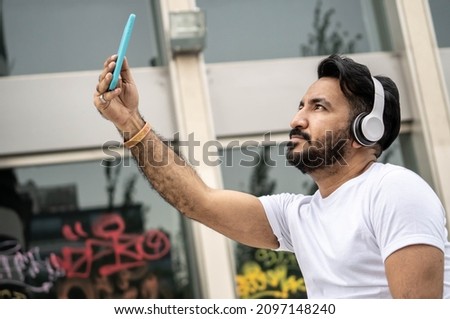 Latin man with beard, taking selfie. In the background walls with spray paint writings.