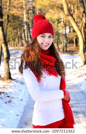 Happy smiling girl in red hat and scarf outdoors in winter park. Winter portrait.