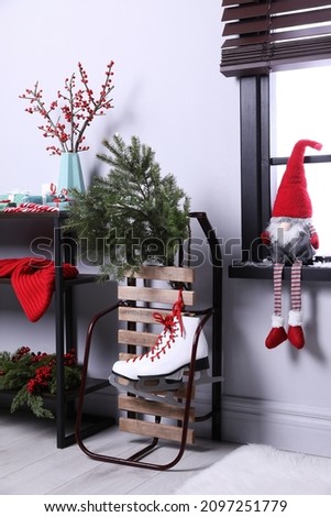 Sleigh with pair of ice skates and fir branches near window in decorated room