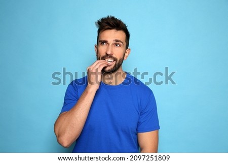Man biting his nails on light blue background