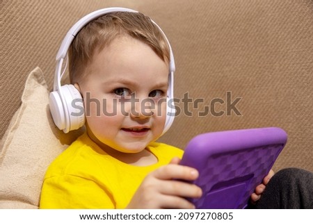 Happy little boy with yellow shirt playing game on digital tablet at home. Portrait of a child at home watching cartoon on violet tablet. Modern kid and education technology.