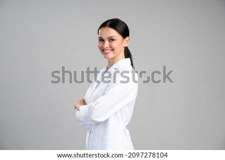 Side view of the smiling female doctor in lab coat with arms crossed looking away and posing against grey background. Medicine concept  Royalty-Free Stock Photo #2097278104