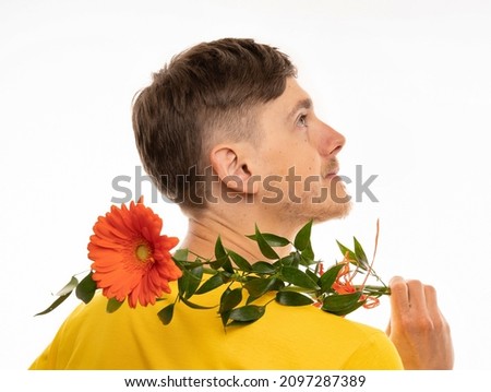 Young handsome tall slim white man with brown hair orange flower on back facing right in yellow shirt isolated on white background