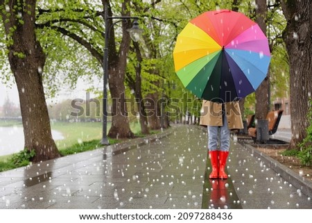 Young woman with umbrella walking in park on rainy day with hail
