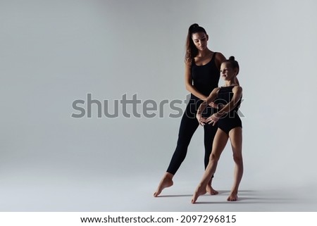 Gymnastic coach helping little girl to do exercise on white background