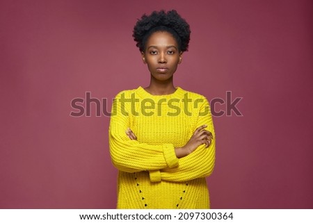 Serious stylish confident young african american girl standing with folded hands, looking at camera on pink background