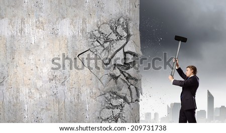 Young businessman breaking cement wall with hammer