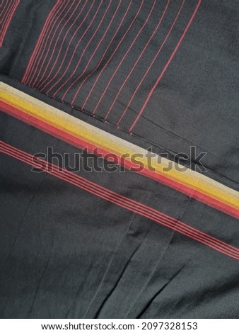 The background of the sarong is black with a combination of yellow and red lines